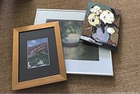 Three artworks grouped together. Two Framed pastels by Eleanor Perkins; one larger white frame (17x14 approx) depicting a boat on the water near trees, and one smaller wooden frame (10x12 approx) with floral landscape. Unframed painting shows textured white flowers in a purple vase.