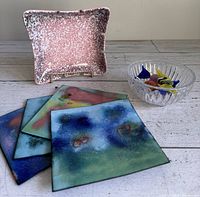 Photo showing pink embossed ceramic ashtray, clear Marquis Waterford crystal bowl with colorful glass candies, and four enamel on copper square trivets with abstract design.