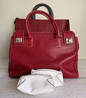 Front view of red leather handbag with two white cosmetic cases in front, showing wear on handbag and cases
