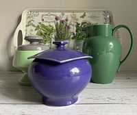 Front view showing the purple pot in front with green footed pot, green pitcher and botanical tray in background
