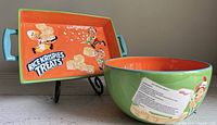 Mixing bowl and serving dish placed together displaying colorful cartoon characters of Snap, Crackle and Pop with Rice Crispies Treats logo on the dish and recipe on the bowl.