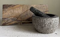 Side view of gray stone mortar and pestle set with marble slab behind, placed on a light-colored surface.