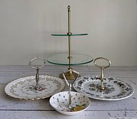 Front view of 3 vintage plated cake plates with metal handles and 2-tier etched glass cake stand with brass poles and finial.