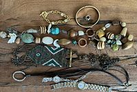 Photo showing diverse jewelry pieces including native beaded necklace with geometric pattern, chunky natural stone necklace, metal bracelets, watches, and leather necklace band.