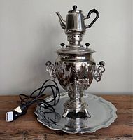 Full front view of the samovar on the matching tray, showing the attached electric cord and plug.
