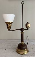 Full side view of vintage brass student desk lamp showing weighted base, single arm with milk glass shade and acorn form detail