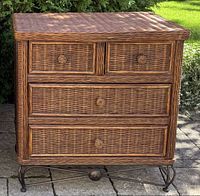 Wicker chest of drawers showing four drawers and top surface with a woven wicker texture and a dark wood frame on a stone patio.