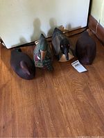 Four duck figurines on wood floor: two wooden decoys (one mallard style) and two fabric ducks.