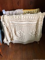 Wooden blanket rack holding two crocheted blankets, one off-white with floral patterns and a second yellow lacy blanket in the background.