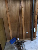 One long copper pipe leaning against wooden wall with blue container nearby and multiple fittings piled on the floor.