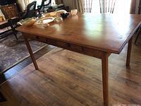 Full view of wooden farmhouse style dining table with objects on top, showing the tabletop and legs.
