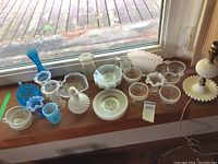 Collection of various hobnail glassware in blue, white milk glass, and clear opalescent glass arranged on a windowsill.
