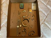Top view of entire lot in cardboard box showing chains, watches, earrings, pendants, and locket