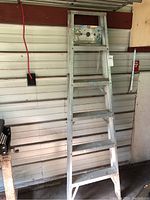 Full view of aluminum step ladder against wall showing entire height and steps. Weathered condition with paint spots and discoloration.
