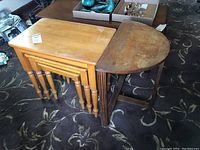 Photo showing three rectangular light wood nesting tables stacked and a demilune side table with wear on top surfaces.