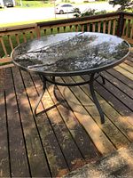 Full view of the round patio table clearly showing the reflective glass top and the metal legs beneath it.