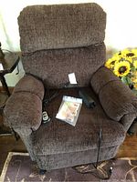 Brown fabric power recliner lift chair with remote and manuals on seat.