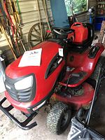Full left-front angle view of tractor showing body, deck, seat, steering wheel and owner’s manual on hood