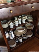 Display of various pieces of Royal Doulton Cranbourne pattern china, including plates, bowls, mugs, creamers, and sugar bowls arranged on wooden furniture