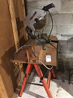 Overall view of Skilsaw chop saw mounted on metal base table with wooden top and power cord visible, placed on orange metal sawhorses.