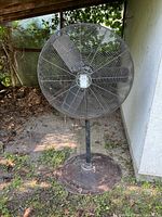 Full front view of Air King standing fan, showing circular protective cage and metal blades outdoors.