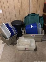 Photo showing multiple beige Rubbermaid storage bins with blue and clear lids, a blue storage container, and stacked green lids behind.