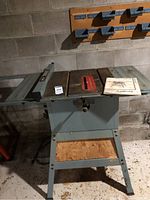Front view of the Delta table saw showing the saw blade opening, tabletop, legs, and fence system in a workshop setting.