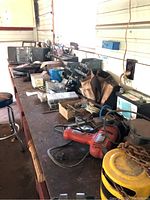 Long workbench with assorted tools including power drill, hand tools, storage boxes, and boom box on a shelf.
