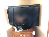 Front view of LG 32-inch TV on wooden table with remote and manual.