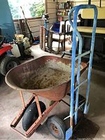 Metal wheelbarrow and blue hand truck side by side in a shed.