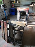 Photo showing folding work bench with metal frame and wooden top, placed on its side revealing construction and wear.