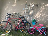 Photo showing adult red Wheeler Trekking 1300 bike and pink and blue kids bike with helmets and background garden ornament attached to wall