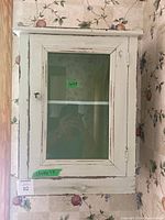 Front view of vintage wooden wall-mounted medicine cabinet with glass door and metal knob.