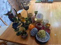 Overview of multiple colorful metal flower-shaped candle holders, decorative shaped candles, and various glass and ceramic holders on a wooden table.