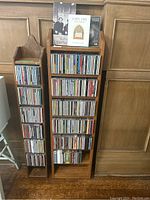 Two wooden vertical shelves with multiple rows of CDs and DVDs, arranged side by side on wooden floor with wood panel background.