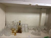 Shelf with an assortment of clear and amber crystal glassware including wine glasses, decanters, vases, and candy dishes
