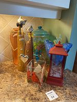 Photo showing six decor items on a kitchen counter: two ceramic cat figurines, a glass beverage dispenser with floral painting, blue ceramic bird, red lantern, and a square glass candle holder.
