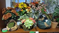 Photo showing several faux floral arrangements with varied flower types and colors, with decorative woven baskets and containers on a shelf.