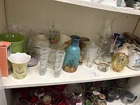 Shelf view of multiple glass and ceramic vases including clear, green, blue-green and yellowish colors