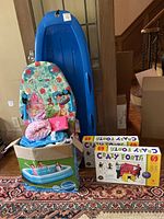 Photo showing blue snow sled, Disney Princess flutter board, inflatable pool, and boxed Crazy Forts sets stacked beside them.
