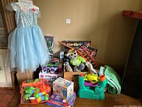 Wide view showing the blue princess dress hanging, stuffed owl toy, Lite-Brite set, toy piano, and other toys and clothes gathered together