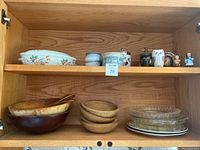Wooden bowls stacked at the bottom shelf, glass plates, ceramic bowls and figurines on upper shelf