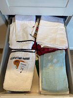 Drawer open showing folded white towels with black trim, embroidered Halloween towel, light blue plush towels, red holiday towel.