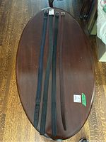 Four men's leather belts laid out lengthwise on a wooden oval table, showing differences in color and wear.