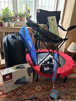 Photo showing folded blue and black camping chair on top of red and black mini trampoline, black push-up grips, blue kite tail, and Outbound double single-high air mattress box.