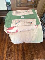 Stacked view of all three pieces including the embroidered quilt, plain comforter, and knitted blanket on wooden floor.