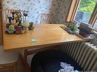 Full view of wood kitchen table with multiple decorative items on top, surrounded by matching chairs and situated near window