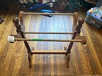 Full view of wooden quilt rack showing three horizontal bars and turned finialed vertical supports on hardwood floor.