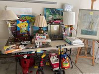 Overview of table with lamps, paintings, art supplies, and children's toys underneath