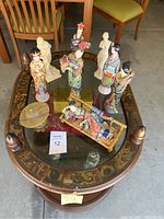 Overview of round wooden side table with glass top, painted panels, assorted figurines and container